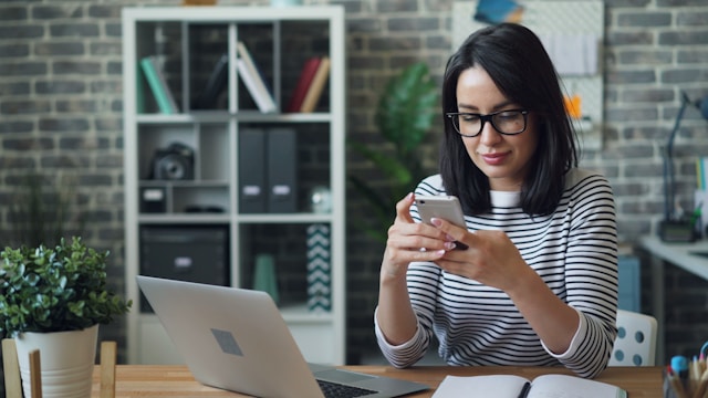 A content creator sits at a table and manages multiple TikTok profiles on her phone and laptop.