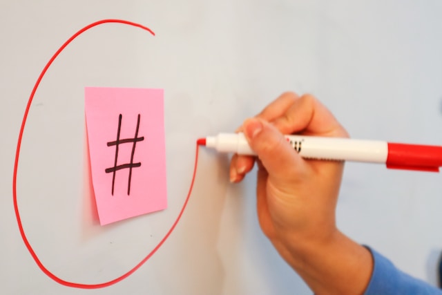 A person draws a circle around a pink sticky note with the hashtag symbol on it. 
