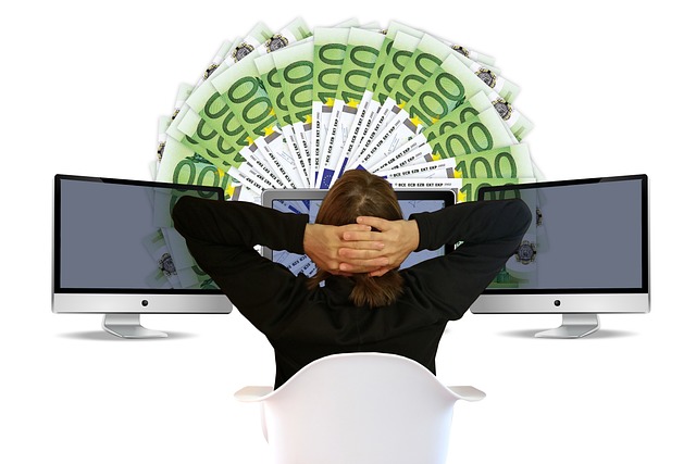 A person sits in front of three computers with notes of cash in front.
