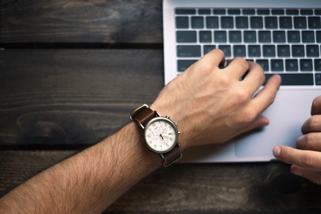 A person checks their watch while using their laptop.
