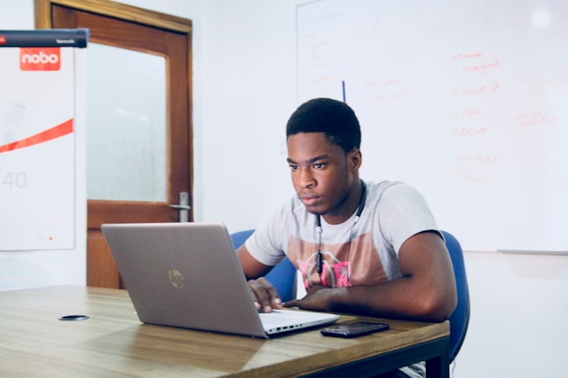 A man sits at a table and looks at his laptop. 