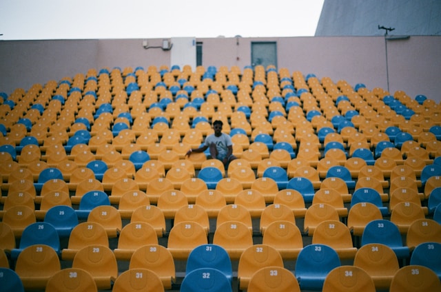 A single person sits in a conference room with dozens of blue and yellow chairs.
