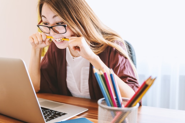 A woman bites a pencil in frustration as she stares at her laptop screen. 
