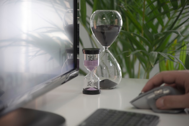 A person works on their laptop beside two glass timers on a table. 