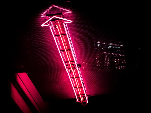 A red neon sign in the shape of an arrow pointing up. 
