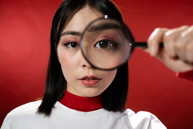 A woman in a red and white sweater holding up a magnifying glass over her eye.