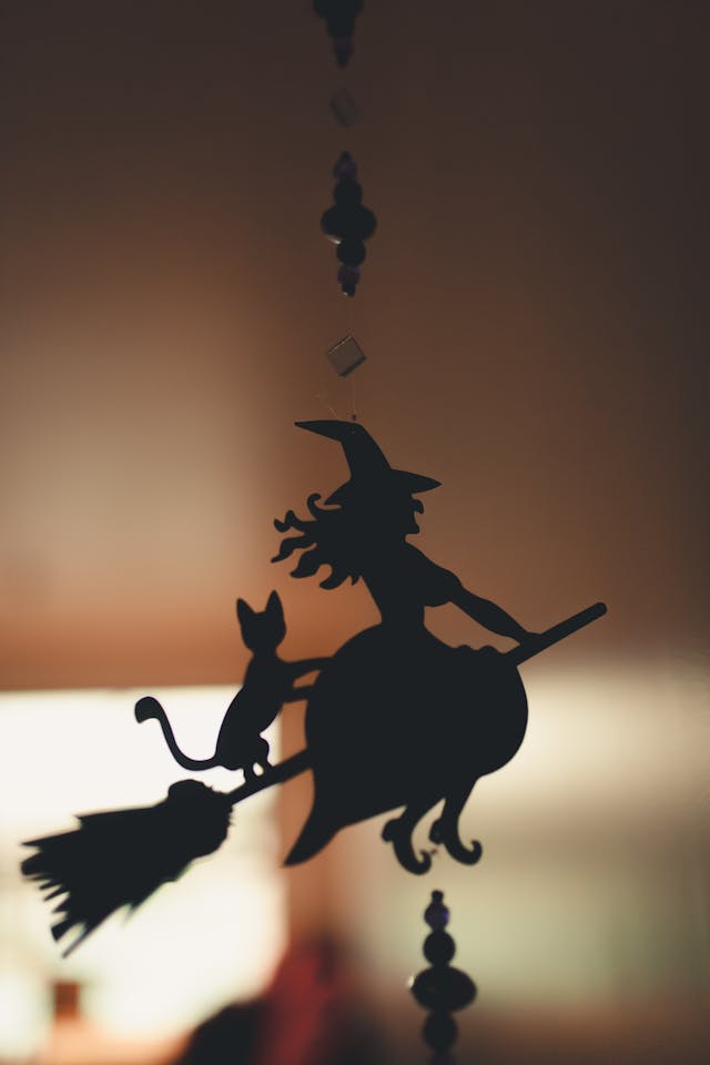 A hanging decoration of the silhouette of a witch flying on a broom with a cat.