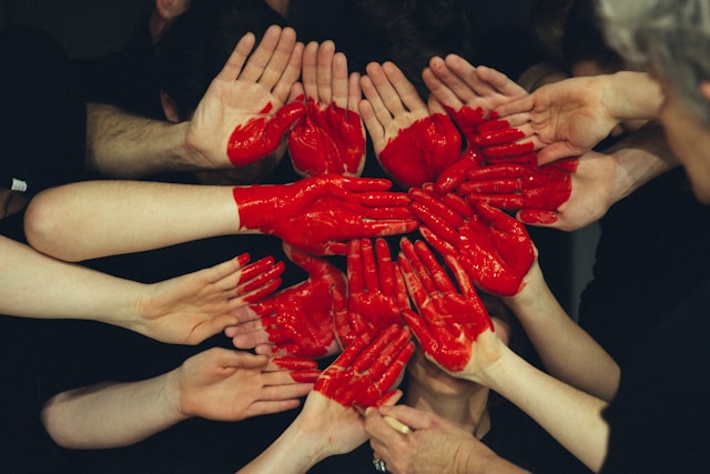 Hands painted red form the shape of a heart. 
