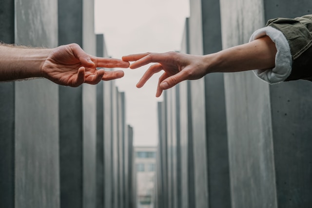 Two people stretching their arms and touching each other’s fingertips. 
