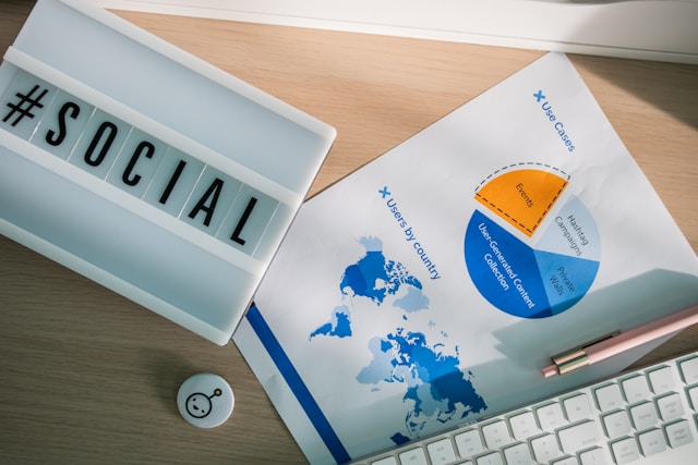 Black and white letter tiles spell the word “#Social” and sit on top of a printed pie chart.