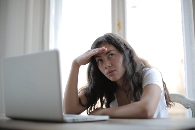 An annoyed young woman rolling her eyes while watching a video on her laptop.