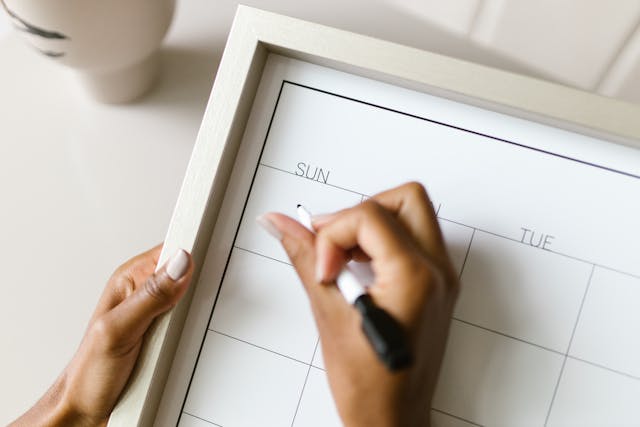 A woman writing on a whiteboard weekly calendar.