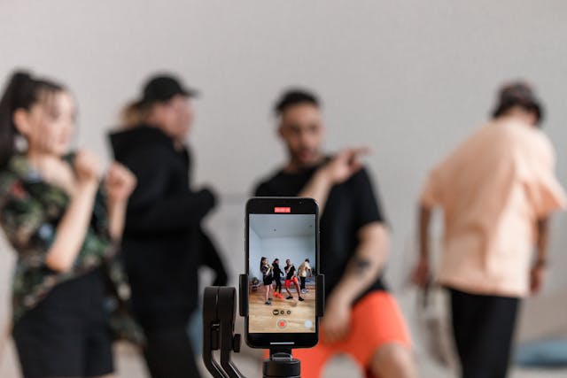 A group of friends dancing and filming a TikTok with a smartphone and tripod.