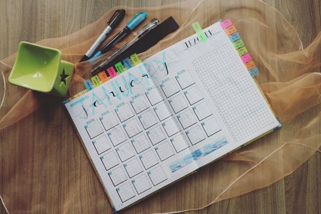 A monthly planner with colorful bookmarks and pens on a wooden table.